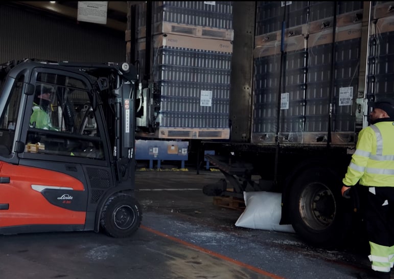 Forklift truck loading pallets onto HGV trailer at warehouse loading bay with safety barriers in place