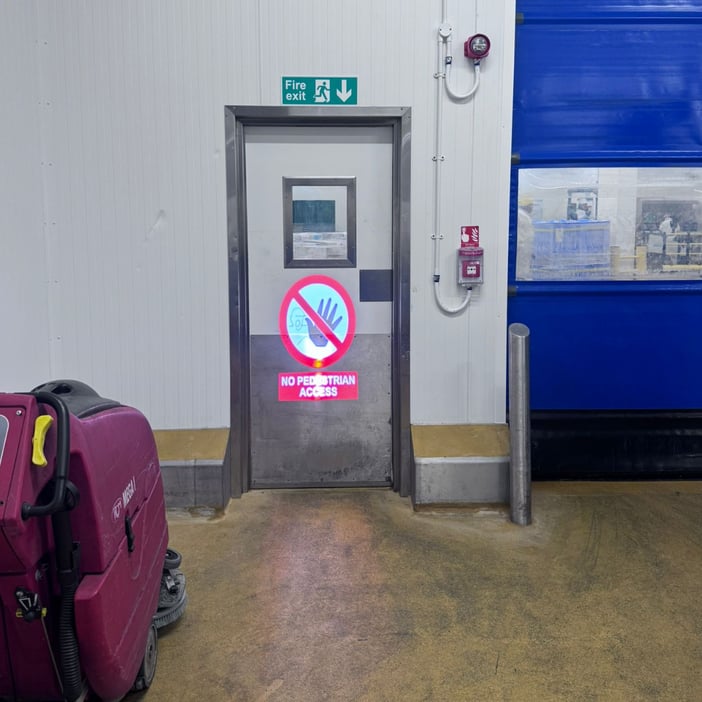 Laser projected floor sign warning of prohibited access zone on warehouse door