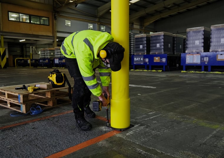 Installer drilling a polymer safety barrier post into a warehouse floor