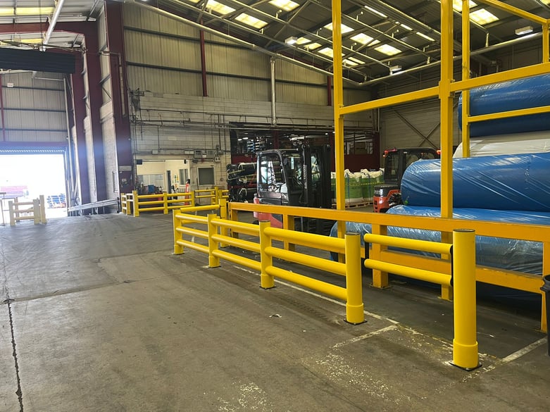 Yellow polymer safety barriers separating pedestrian walkway from FLT route in UK warehouse with material racking