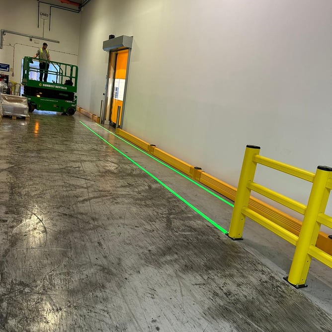 Worker on scissor lift operating safely alongside polymer barriers and LED projected floor walkway