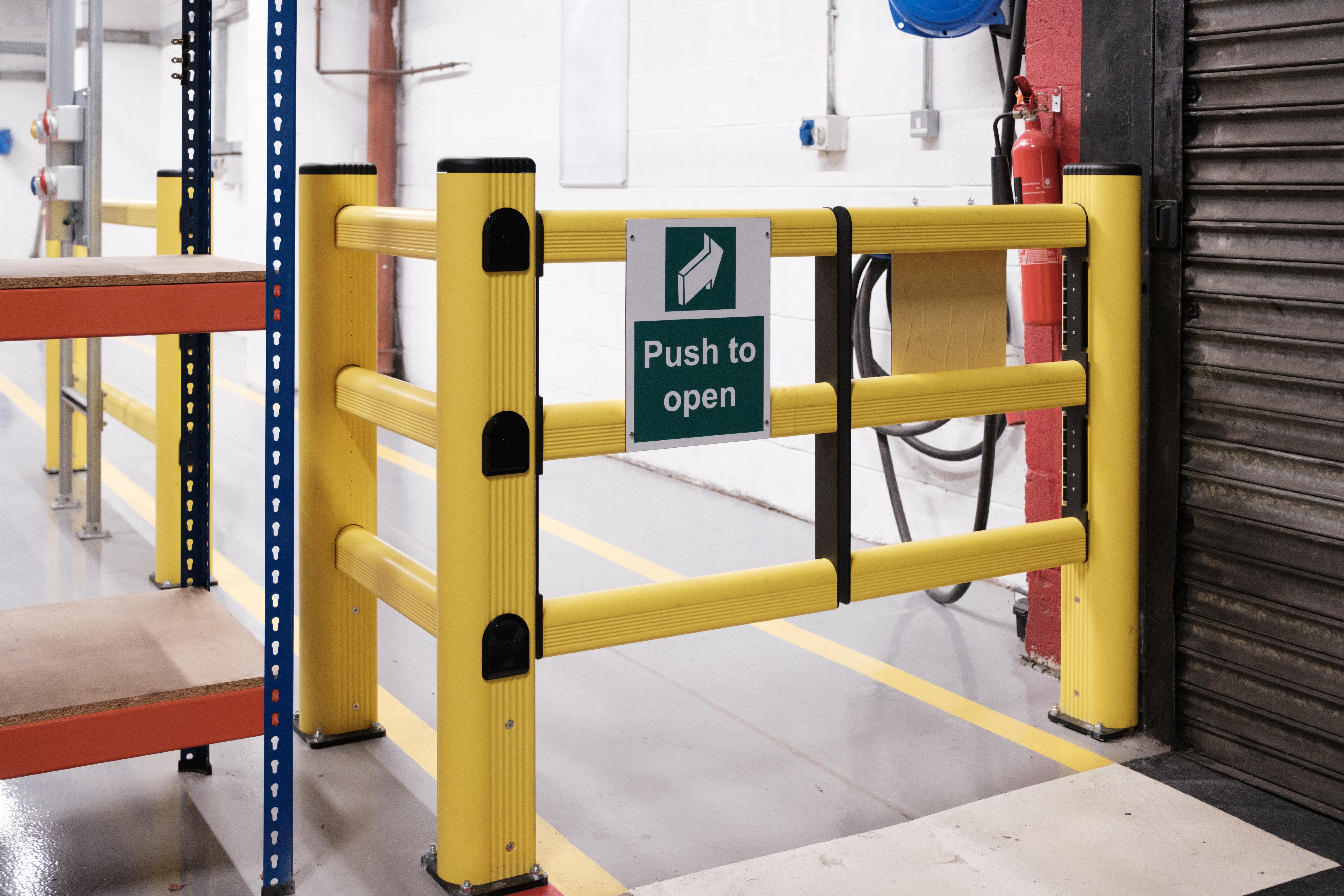 Yellow polymer safety gate providing controlled pedestrian access through warehouse safety barriers"