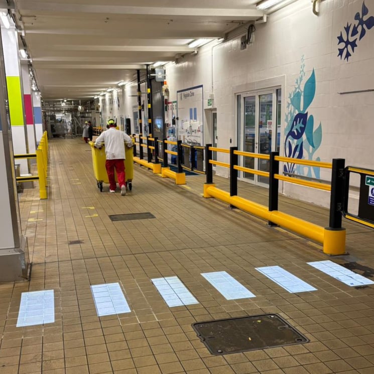 Warehouse operative pushing waste bin past LED pedestrian crossing point in UK distribution centre